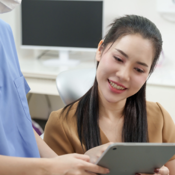 Smiling female dental patient reviewing follow-up treatment plan on a tablet with her dentist after an emergency procedure.