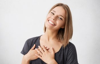 Beautiful positive friendly-looking young mixed race woman with lovely sincere smile feeling thankful and grateful, showing her heart filled with love and gratitude holding hands on her breast